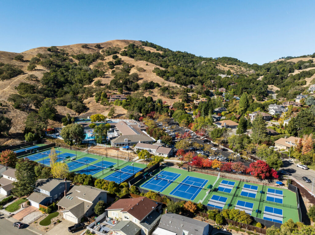 Aerial view of 8 tennis courts and 6 pickleball courts at Bay Club Rolling Hills in Novato. The tennis courts have been resurfaced using Plexipave acrylic resurfacer in dark blue and medium green. The pickleball courts were converted from 2 tennis courts. The pickleball courts' play area is dark blue, the kitchen is gray and the perimeter is medium green using Plexipave Acrylic surfacer