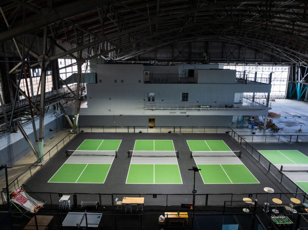 Aerial view of the indoor pickleball courts at Bay Padel on Treasure Island in San Francisco. The pickleball courts' black perimeter and grey kitchen were surfaced using Sportmaster acrylic resurfacer. The play area was surfacced using Plexipave acrylic resurfacer in light green.