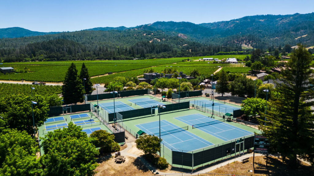 Five tennis courts and Four pickleball courts that were converted from a tennis court at Crane Park in St. Helena. The pickleball and tennis courts were reconstructed using the slipsheet overlay method and surfaced with Plexipave acrylic resurfacer in Dark Blue and Dark Green with white striping. The background shows a vineyard and tree filled hills.
